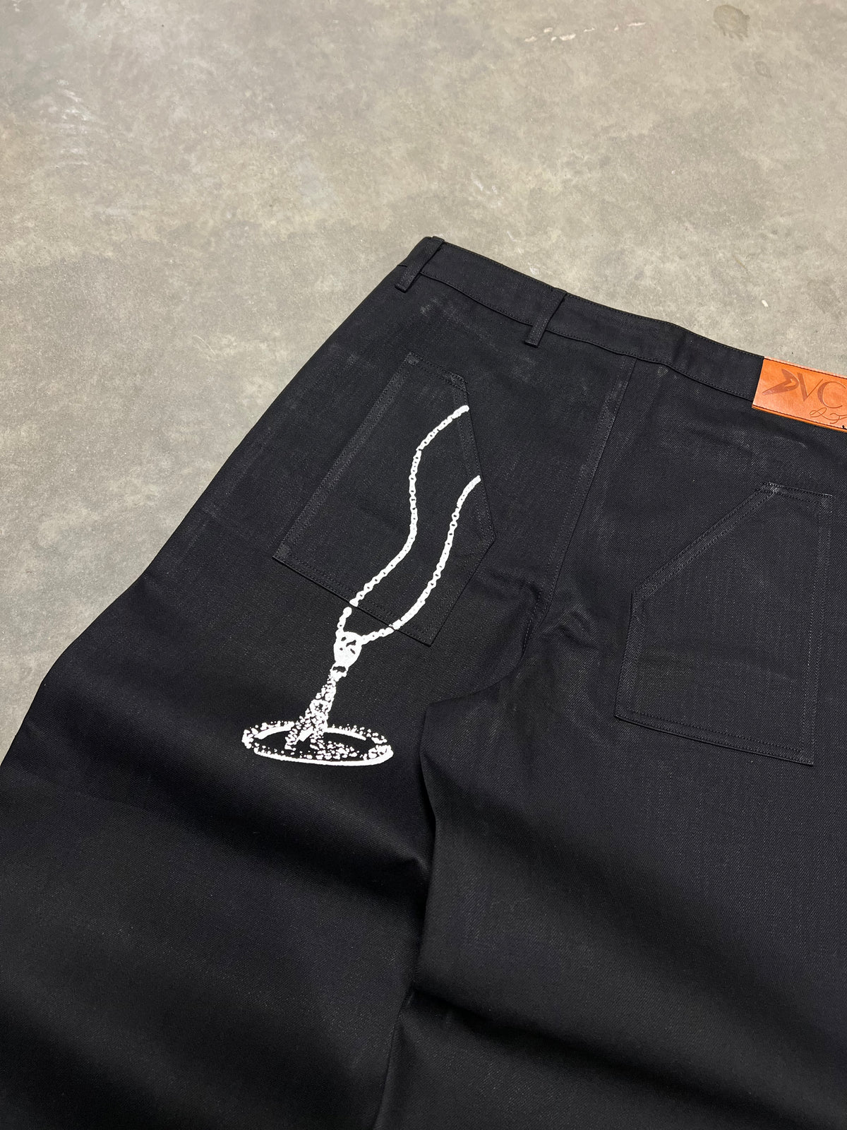 Jean noir signature DIVICE – détail du collier DIVICE dessiné sur la poche arrière et étiquette en cuir orange