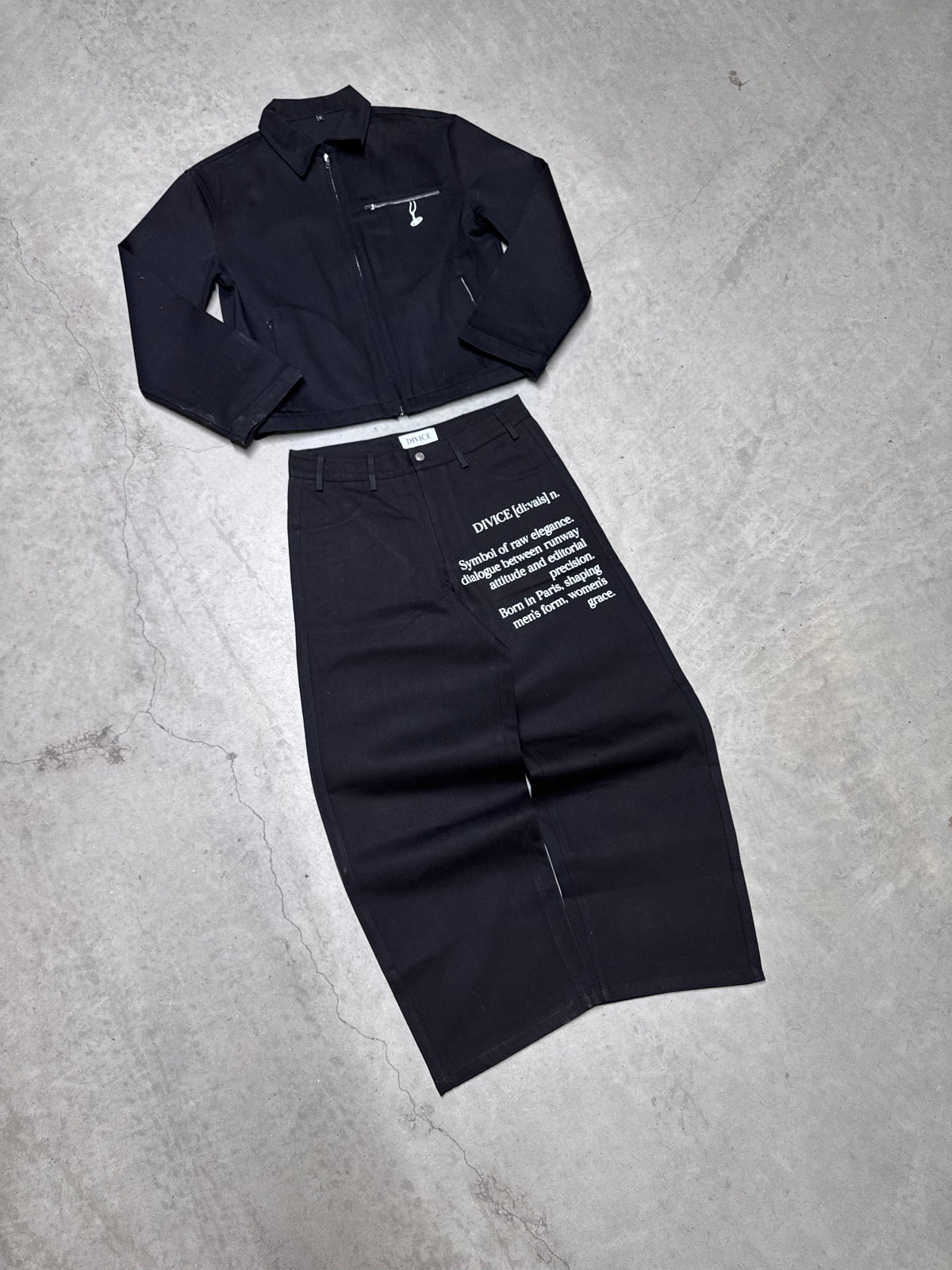 Veste noire signature DIVICE – posée à plat avec le jean noir