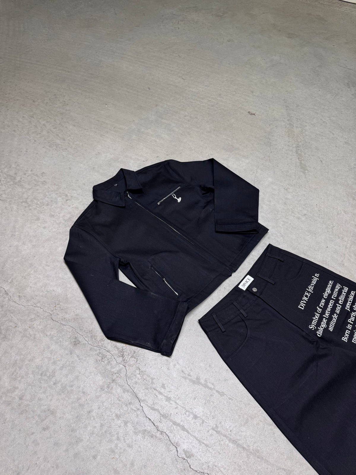 Veste noire signature DIVICE – posée à plat, poche zippée et col chemise