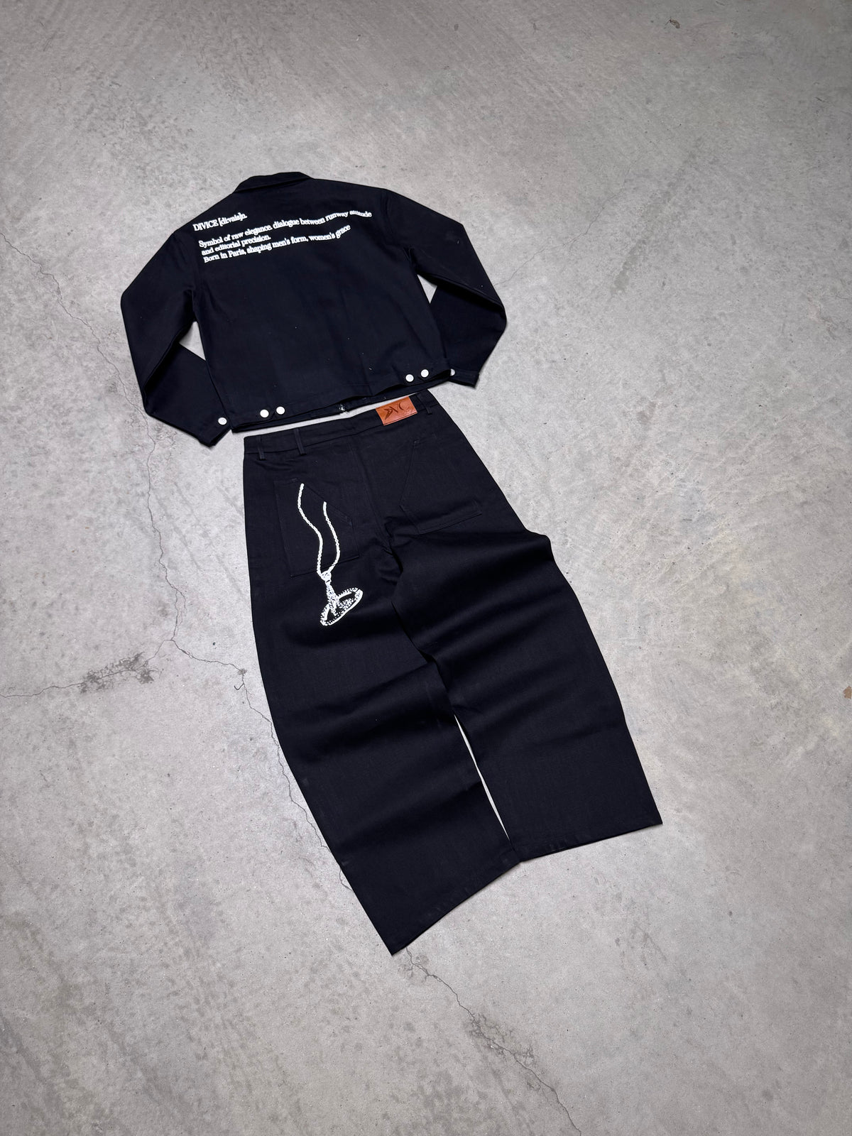 Veste noire signature DIVICE – posée à plat avec le jean noir